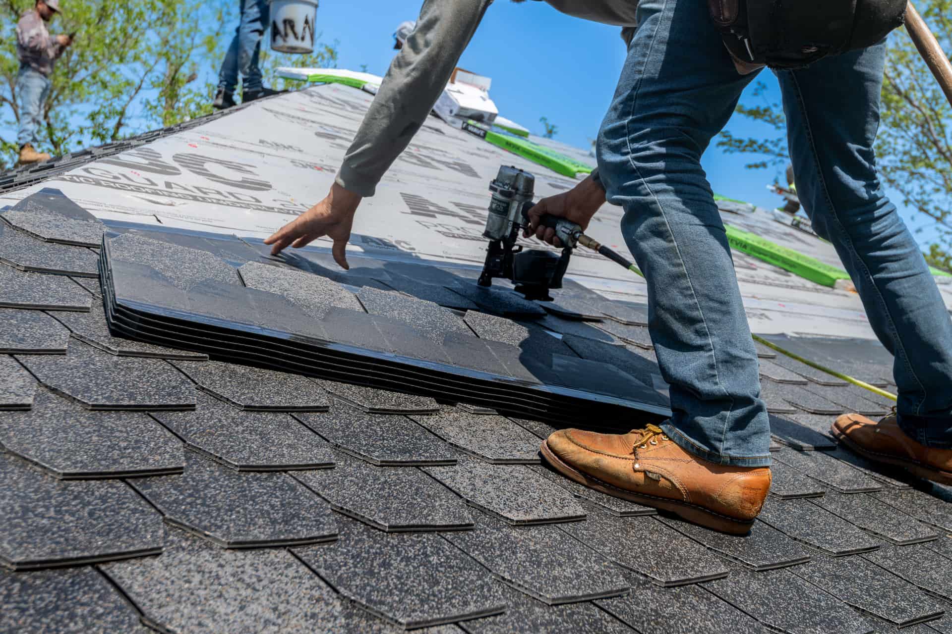 Roofer fastening a course of asphalt shingles over synthetic underlayment on a residential roof