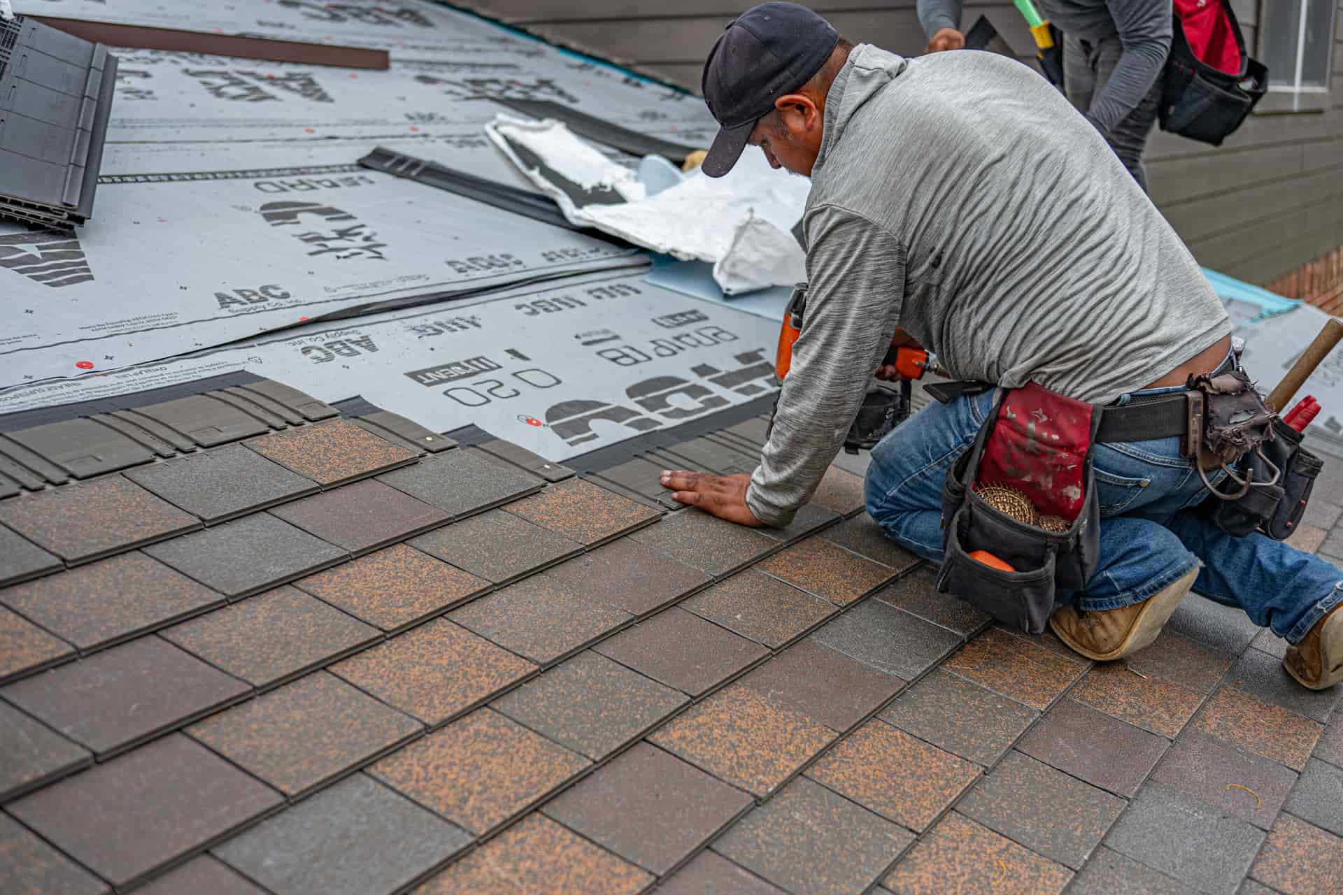 Roofer laying a course of laminated asphalt shingles across a residential roof deck